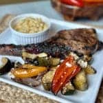 Roasted vegetable salad with a pork chop and mac and cheese on a plate.