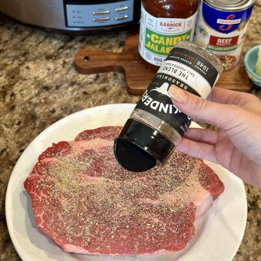 Seasoning a chuck roast with salt, pepper and garlic powder.