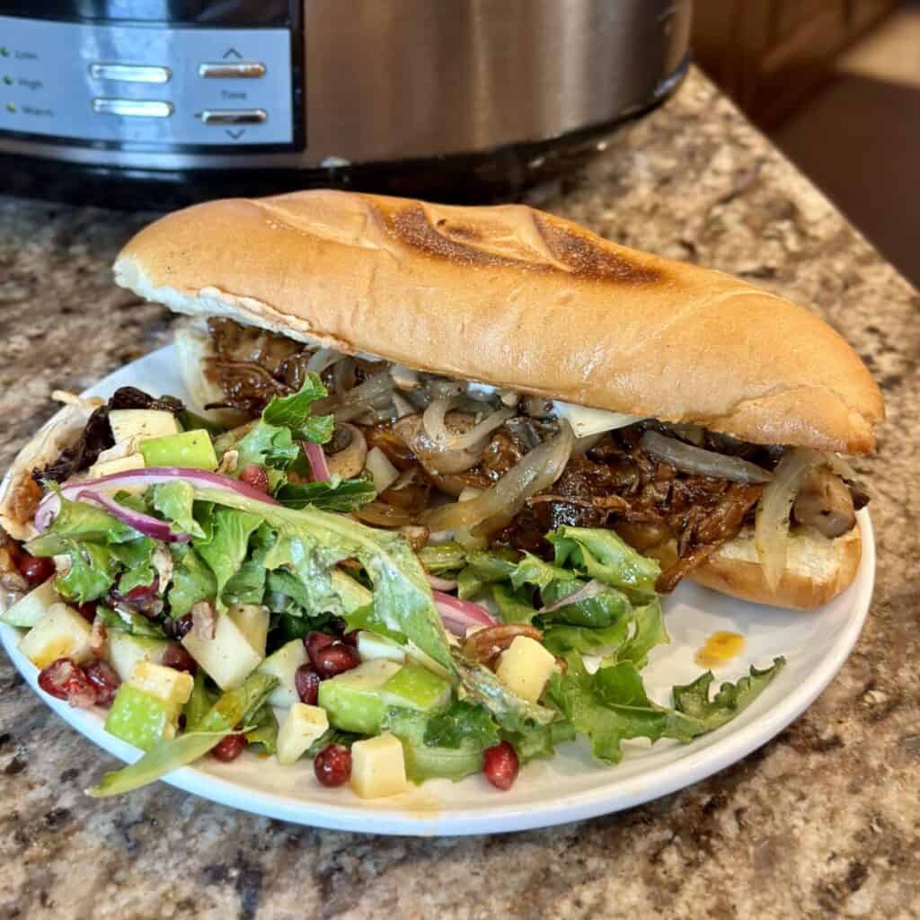 A slow cooker barbecue beef sandwich on a plate with a salad.