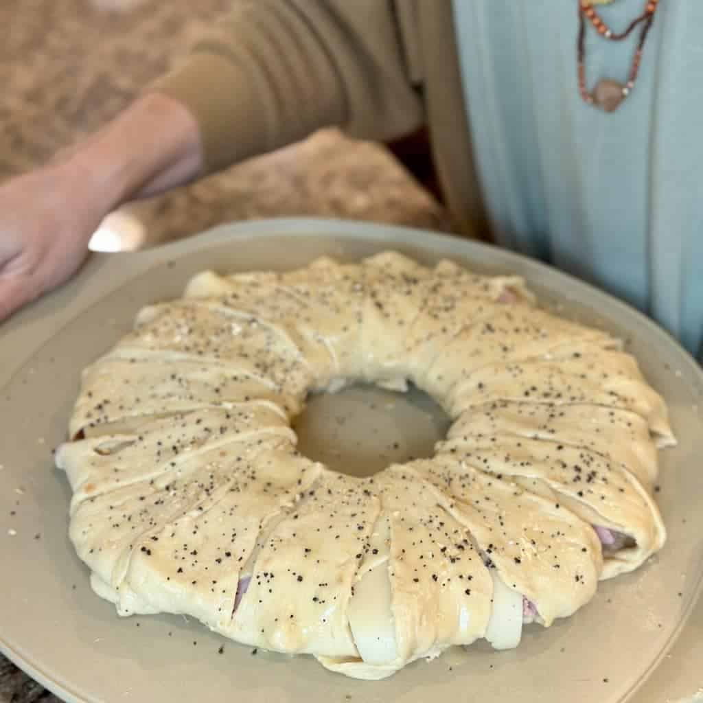 A pizza stone topped with an assembled ham and swiss crescent ring roll.