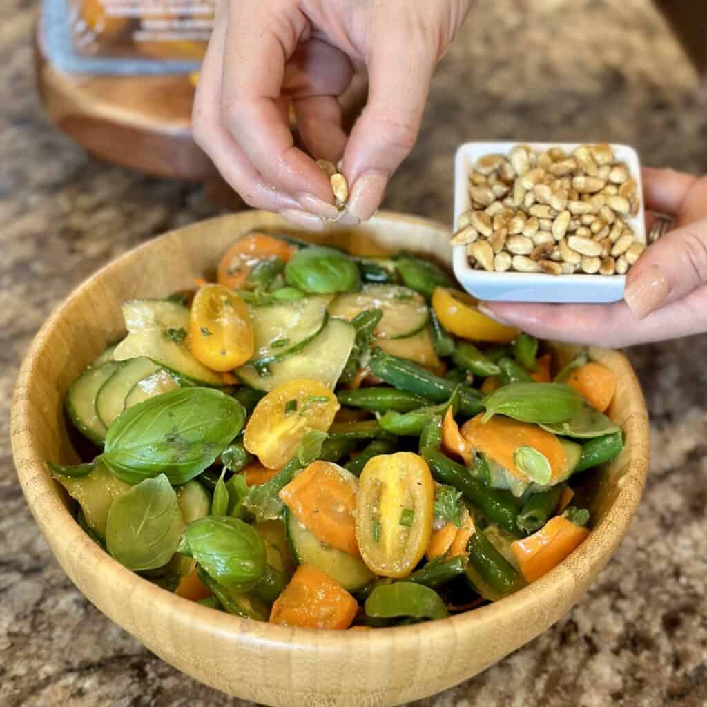 Adding pine nuts to the top of green bean salad.