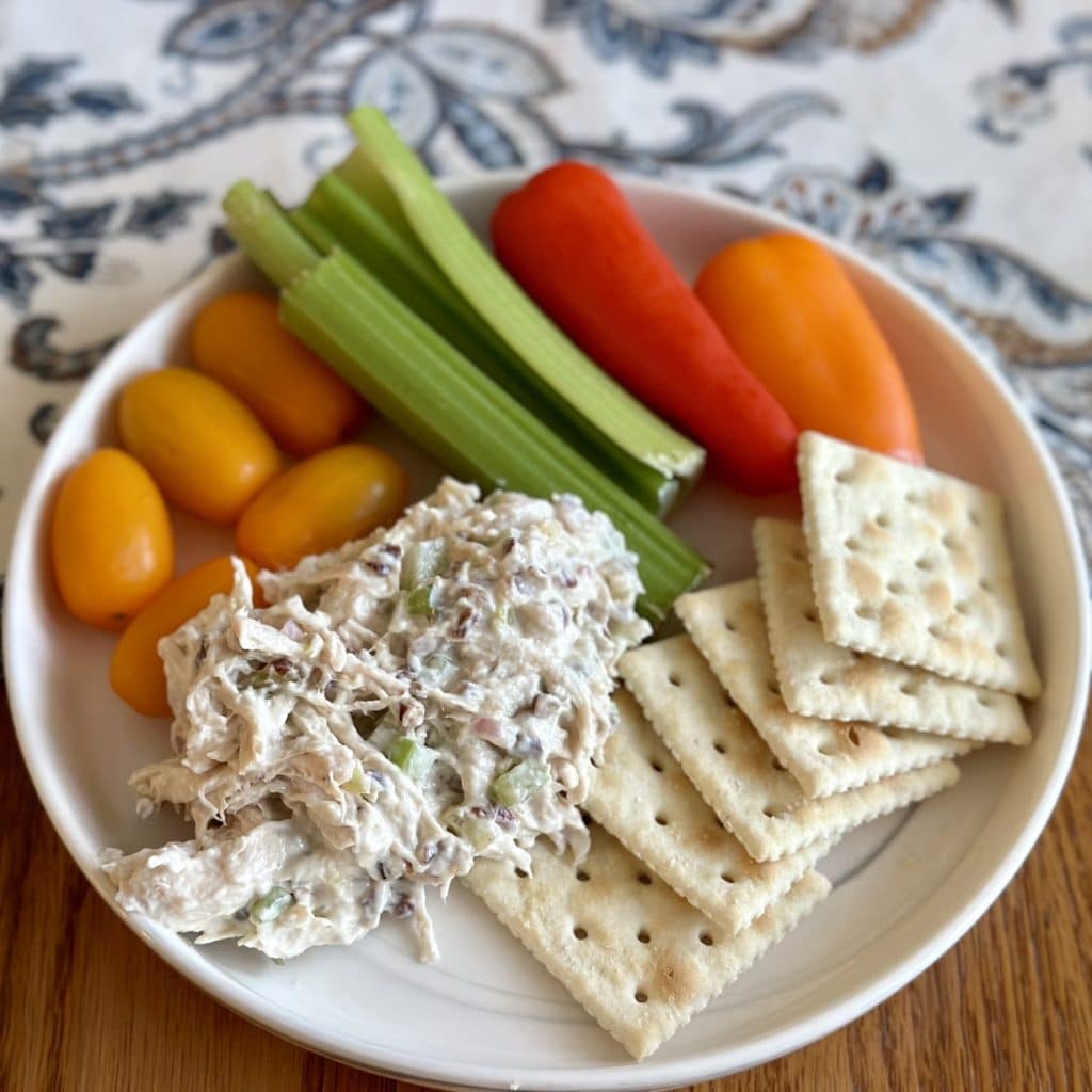 A plate of chicken salad, crackers and veggies.