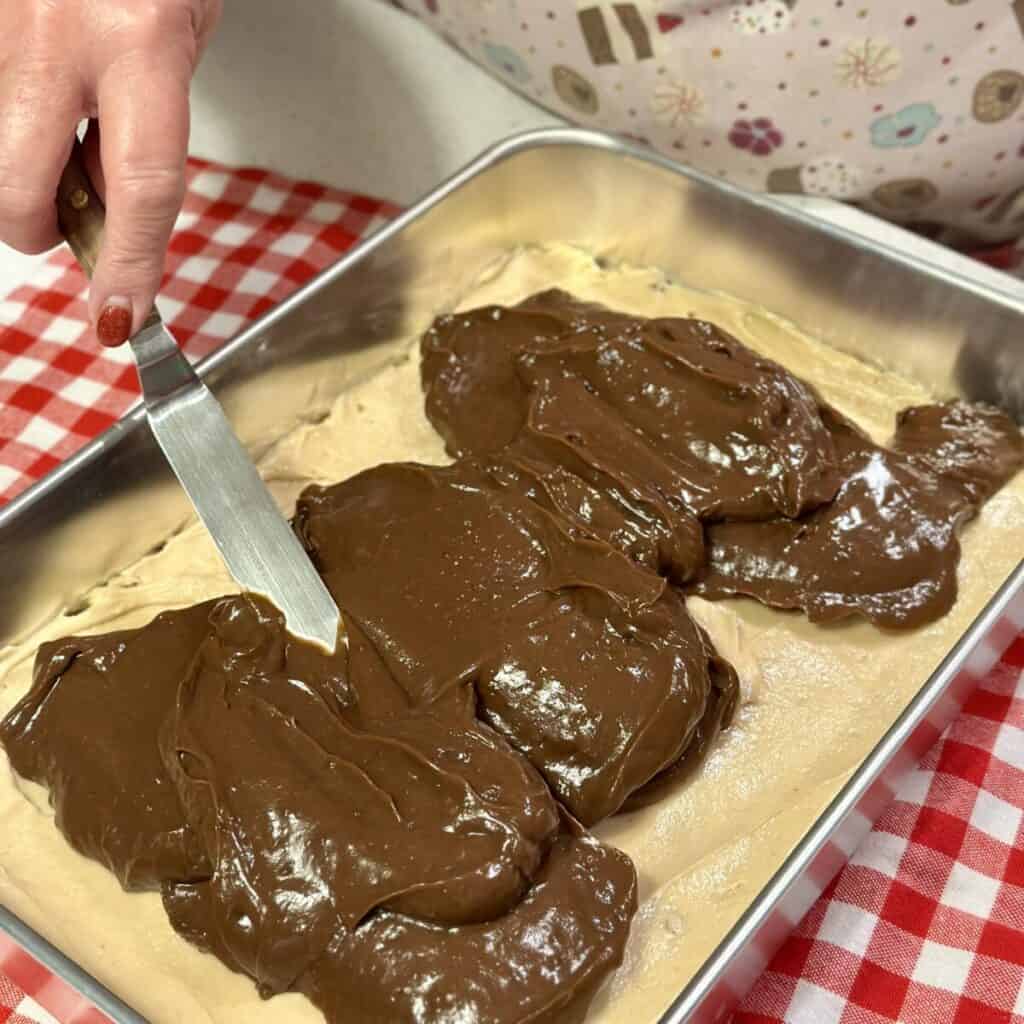 Spreading chocolate pudding on a peanut butter layer of a dessert.