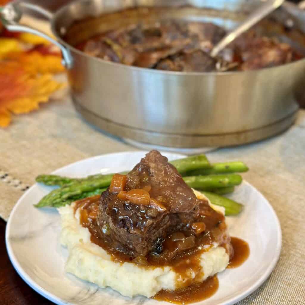 A plate with mashed potatoes, asparagus and braised short ribs.