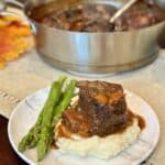 A plate with mashed potatoes, asparagus and braised short ribs.