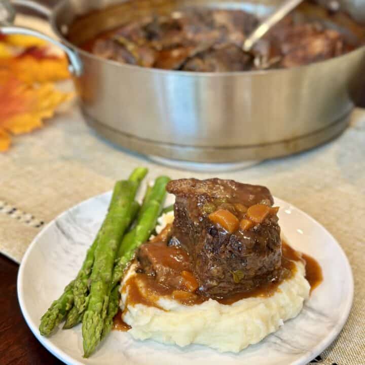 A plate with mashed potatoes, asparagus and braised short ribs.