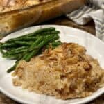 A serving of french onion chicken and rice bake on a plate with green beans.