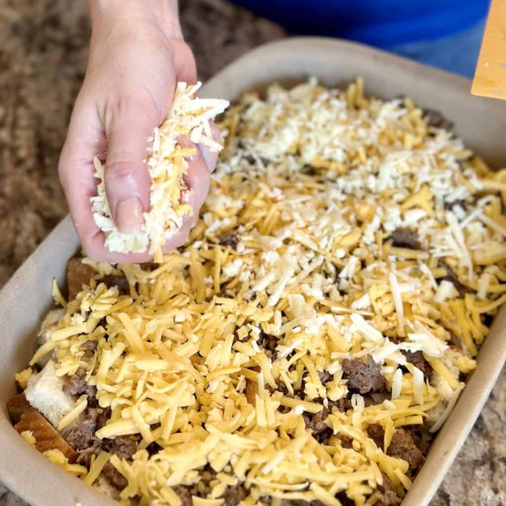 Adding shredded cheese to the top of a breakfast casserole.