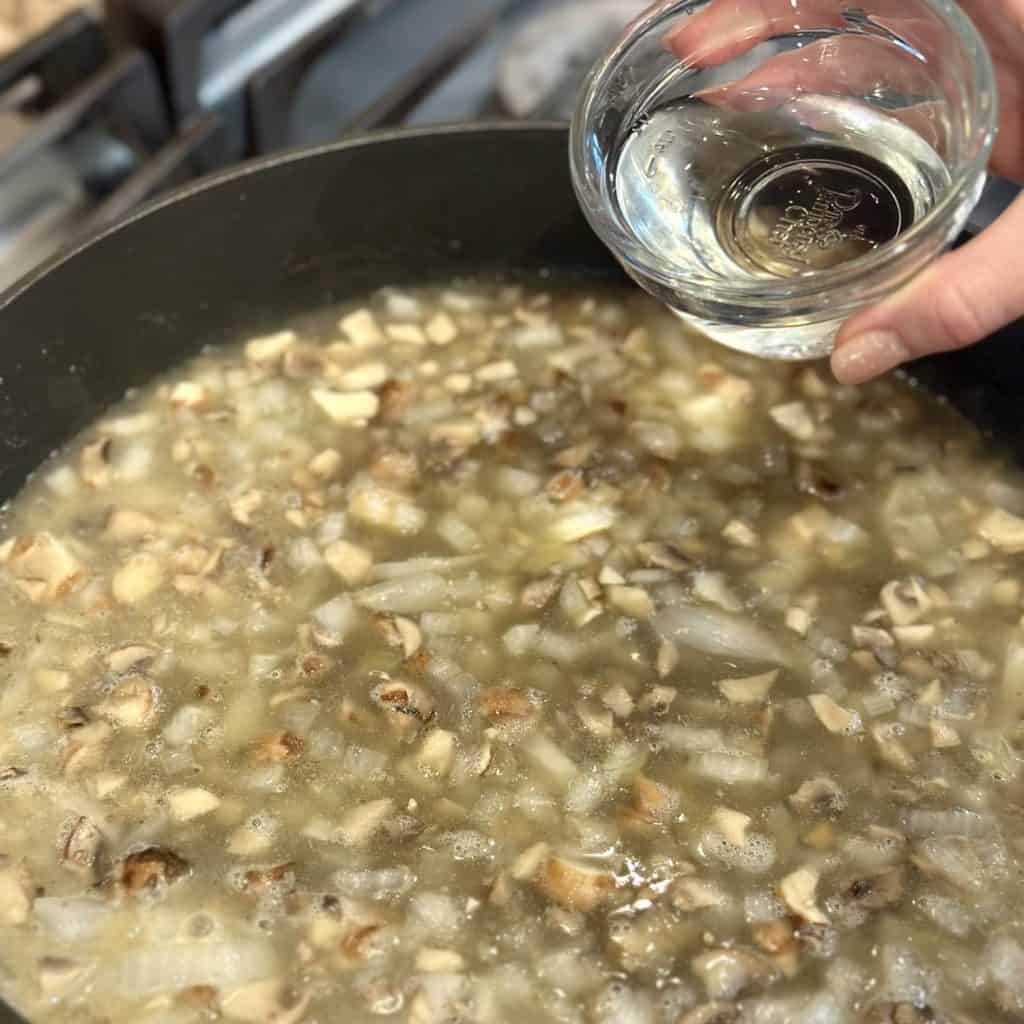 Adding water and broth to a pan of vegetables.