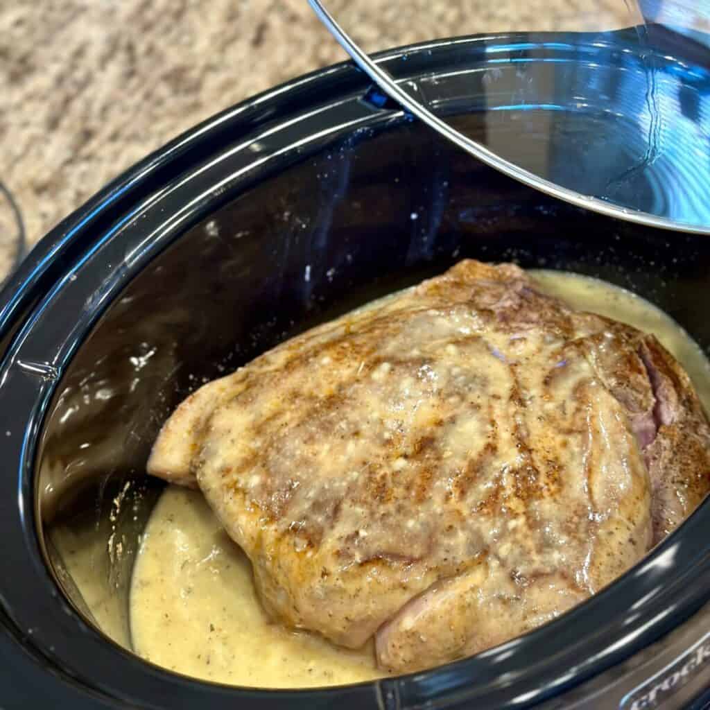 Adding a pork roast to a crockpot.