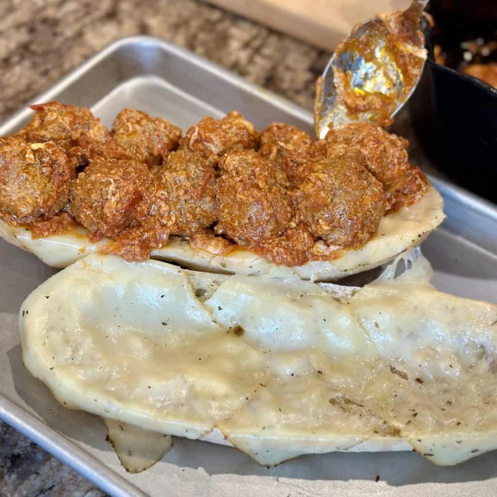 Spooning meatballs on a sub sandwich.