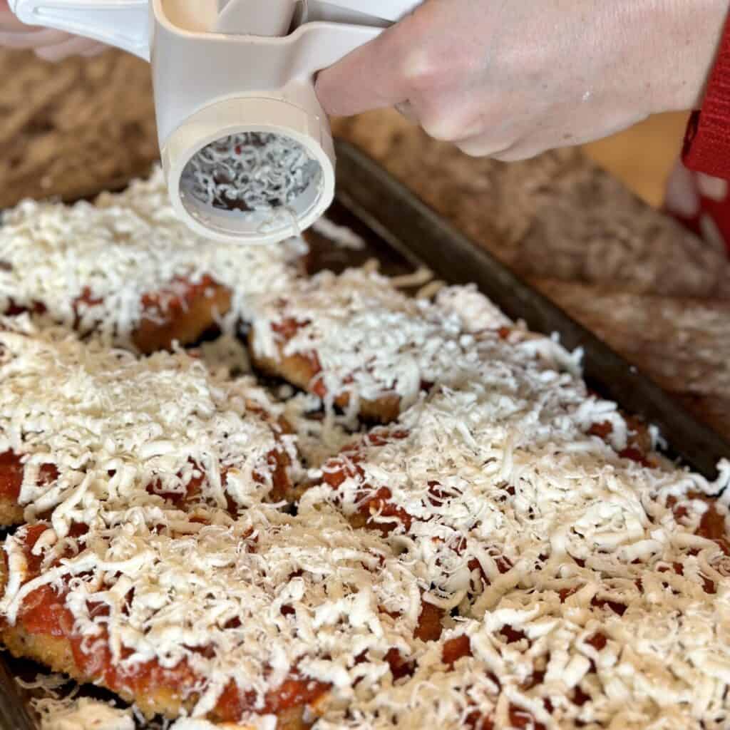 Adding parmesan to the top of chicken parmesan.