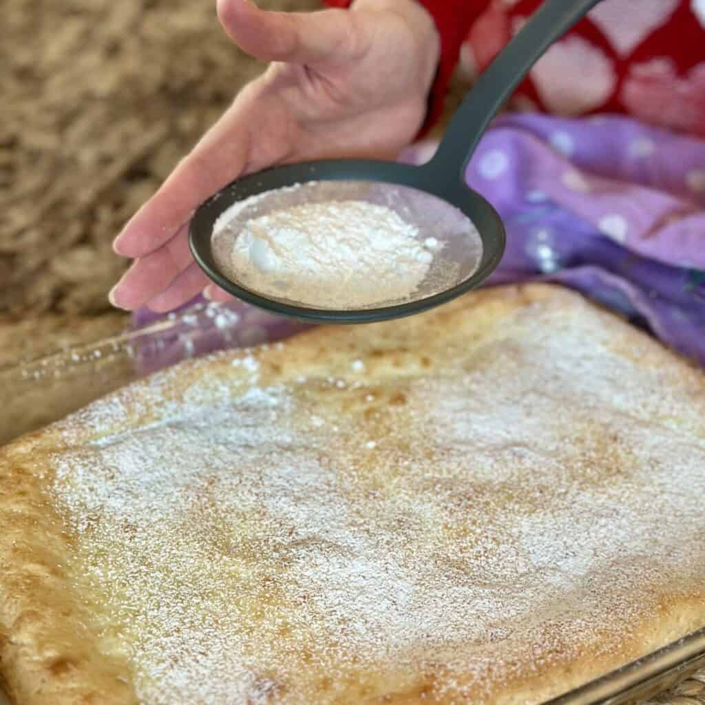 Sprinkling powdered sugar on yum yum bars.