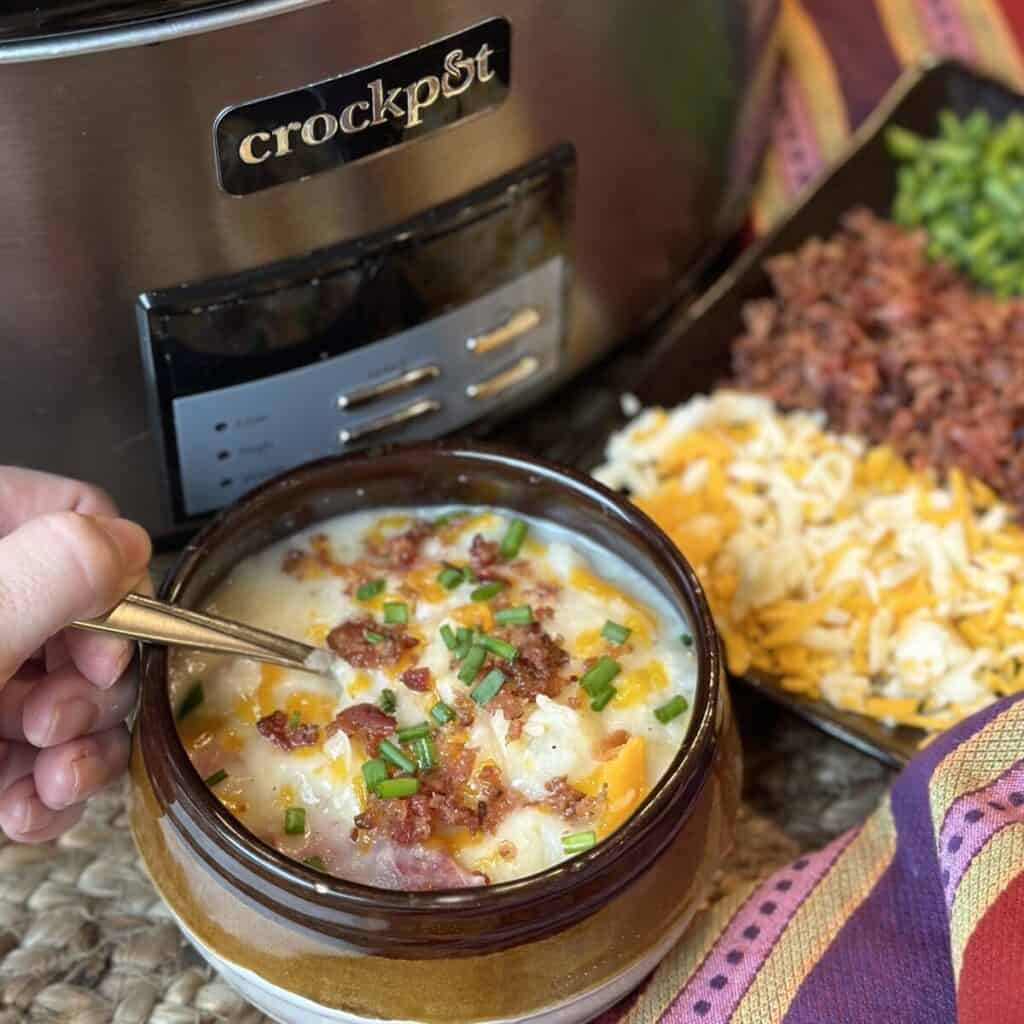 Getting a spoon of potato soup from a bowl.