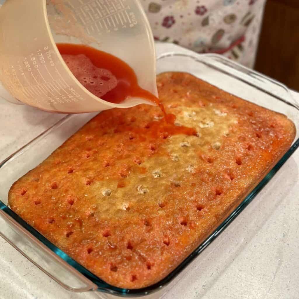 Pouring raspberry gelatin on cake.