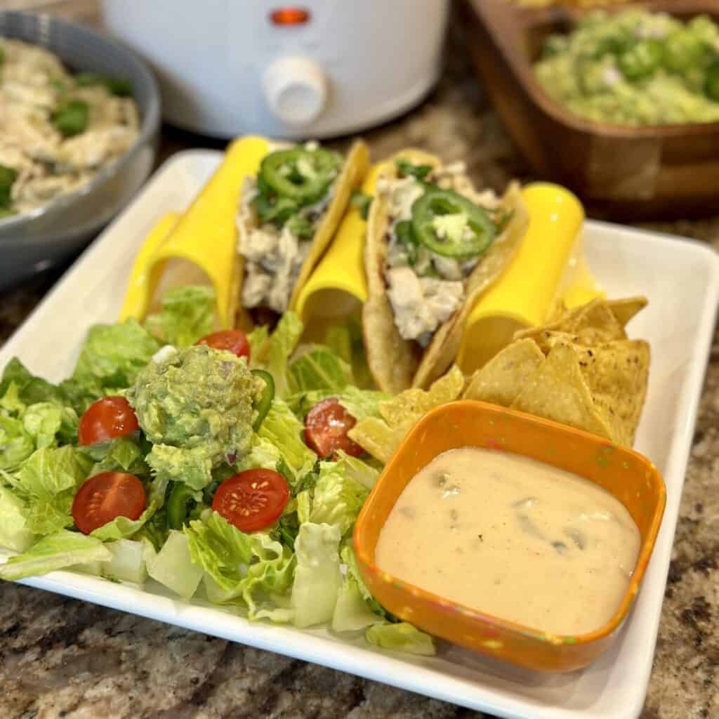 A plate of green chili chicken tacos, cheese dip and salad.