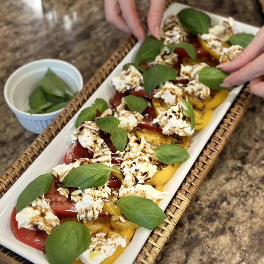 Adding basil to the top of burrata and tomatoes.