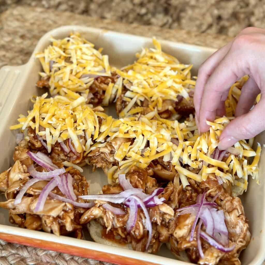 Adding chicken, cheese and onion to buns in a pan.