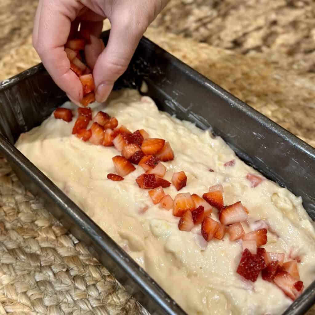 Adding strawberries to the top of a pound cake.