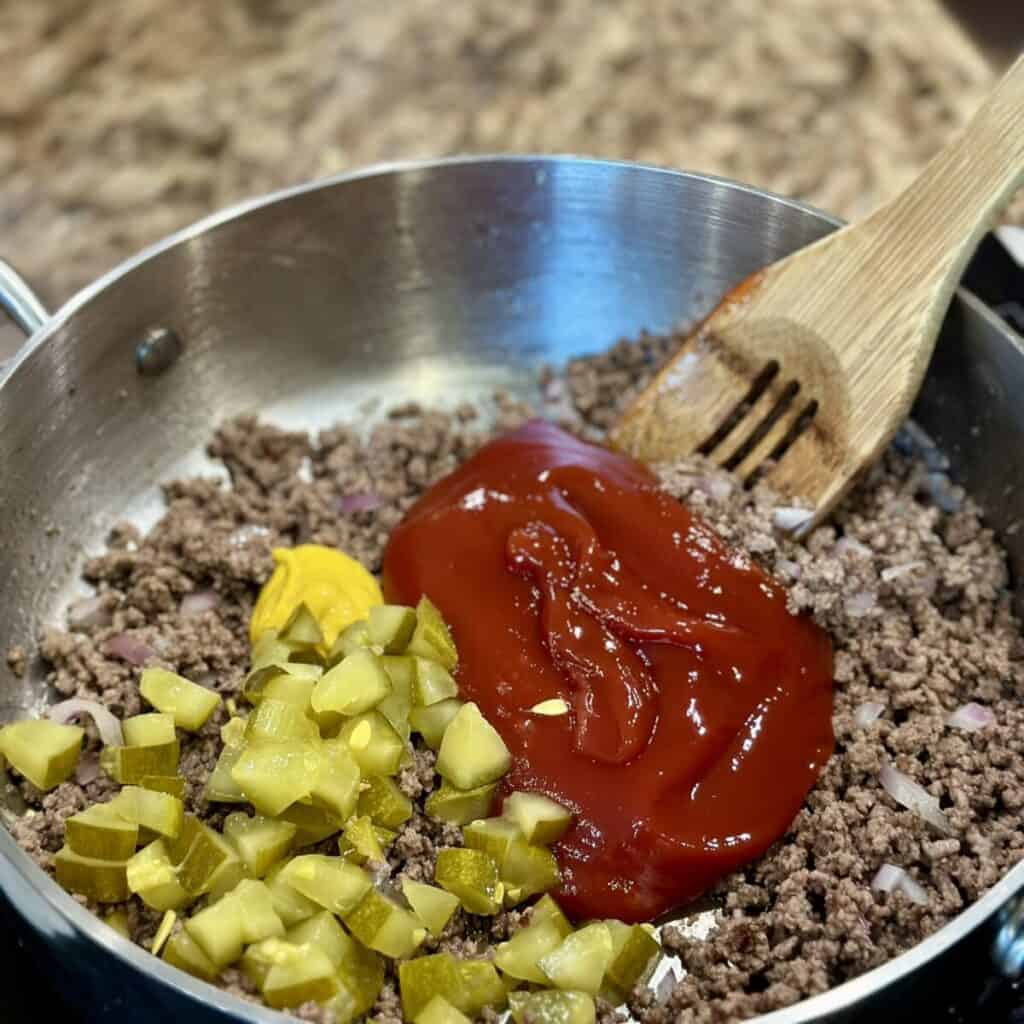 Mixing ketchup, mustard and pickles into beef.