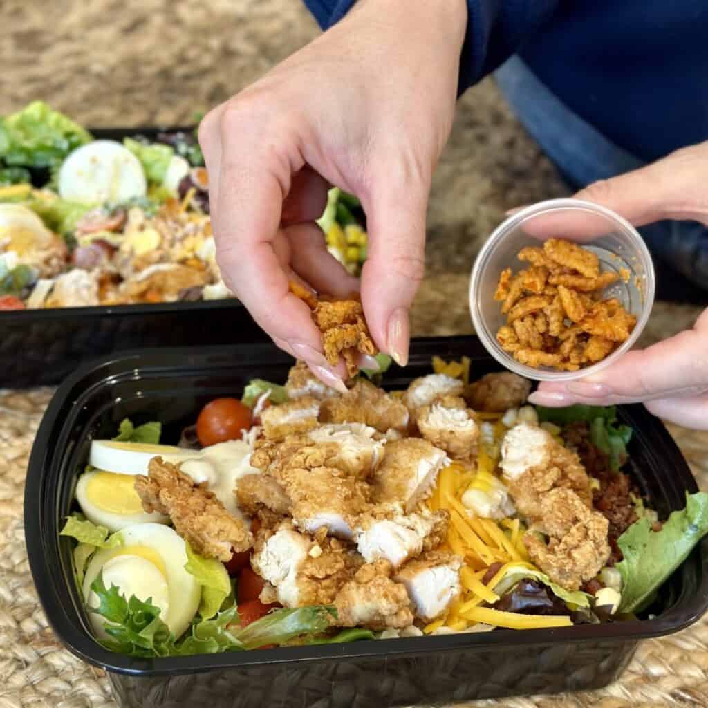 Adding crispy red peppers to the top of a salad.