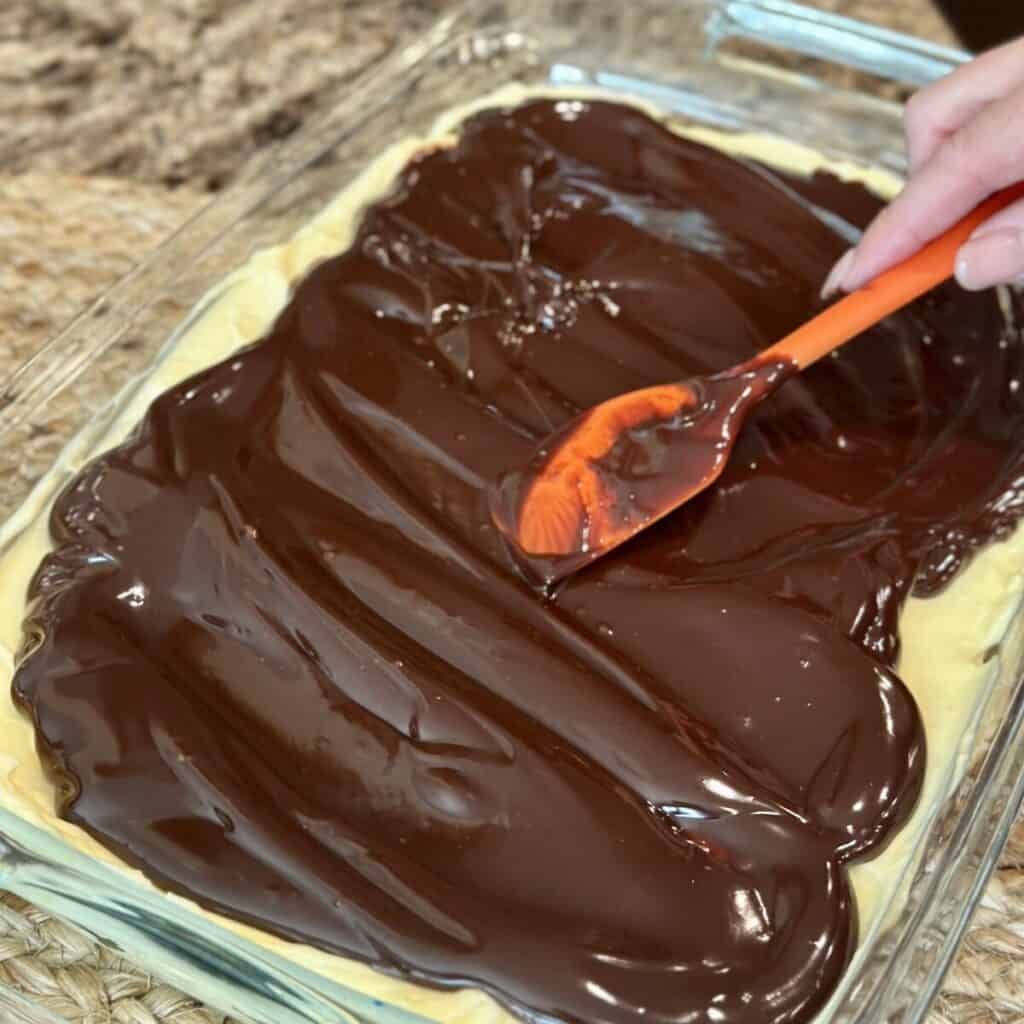 Spreading chocolate ganache on an eclair cake.