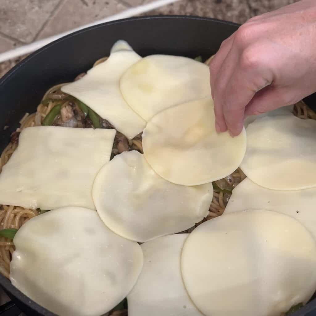 Adding cheese to the top of cheesesteak pasta.