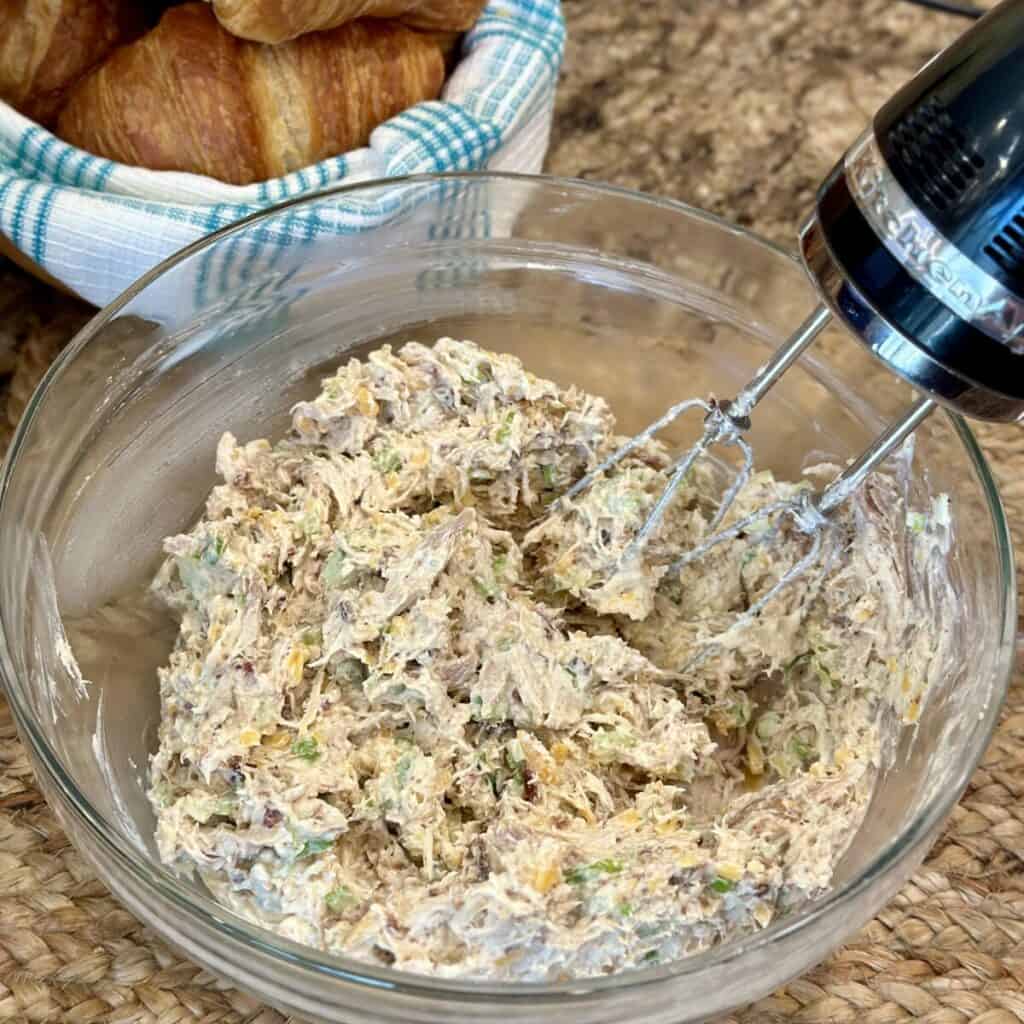 Mixing together chicken salad in a bowl with a mixer.