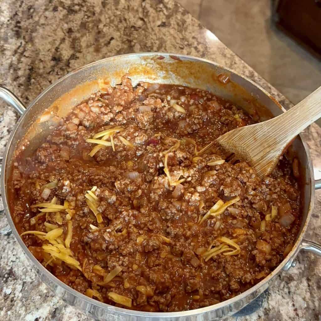 Stirring manwich sauce in to beef in a skillet.