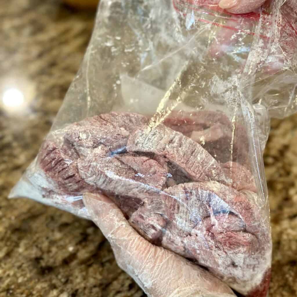 Coating flank steak in cornstarch in a bag.