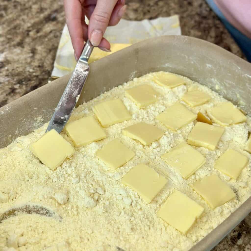 Adding butter to the top of a cake mix in a baking dish.