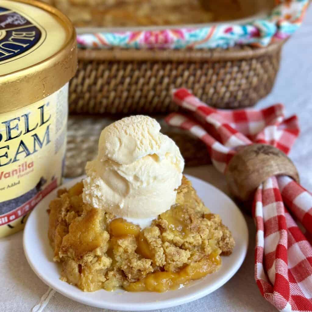 Ice cream topped peach cobbler on a saucer.