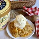 A plate of peach cobbler next to a gallon of ice cream.