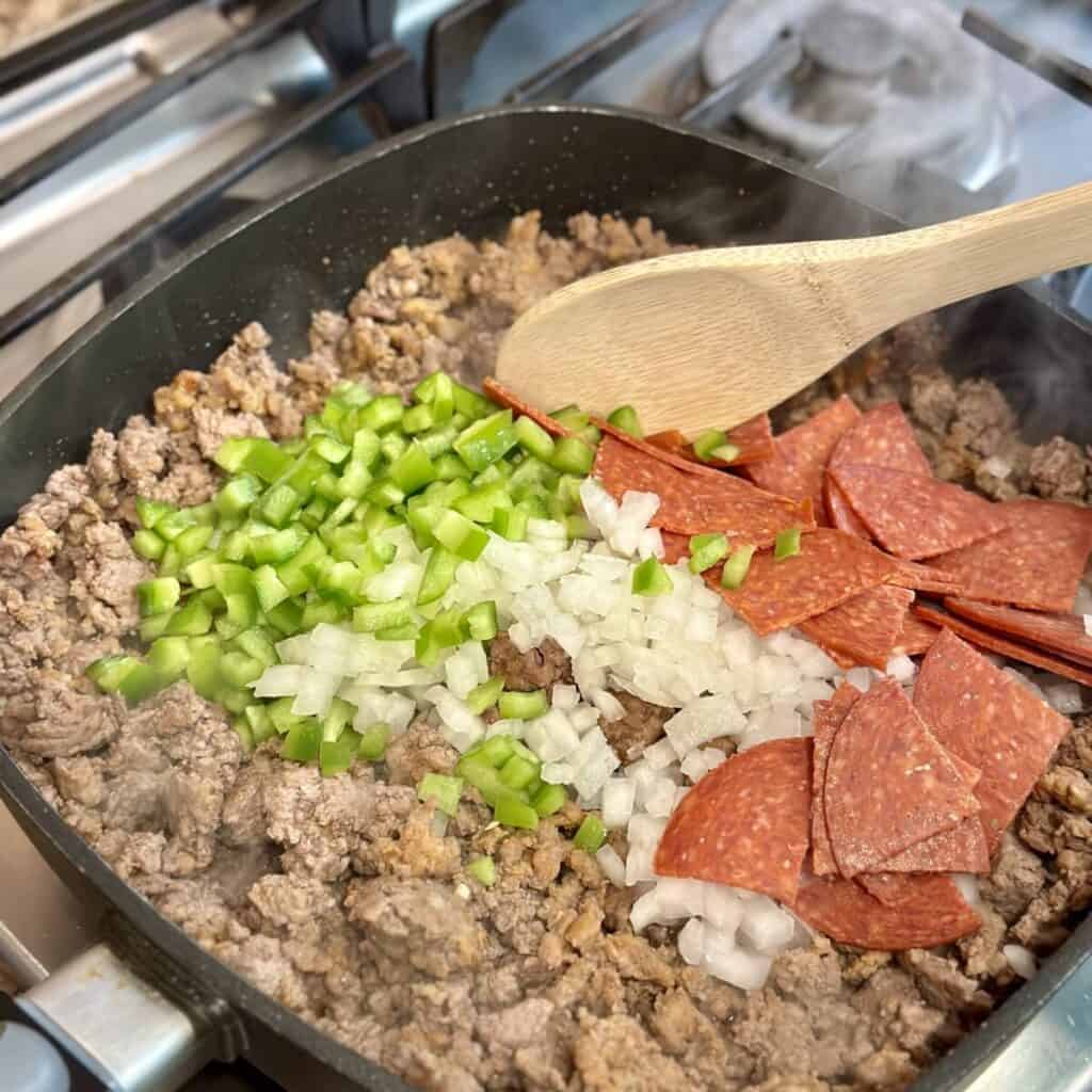 Mixing together ground beef, pepperoni and veggies in a pan.