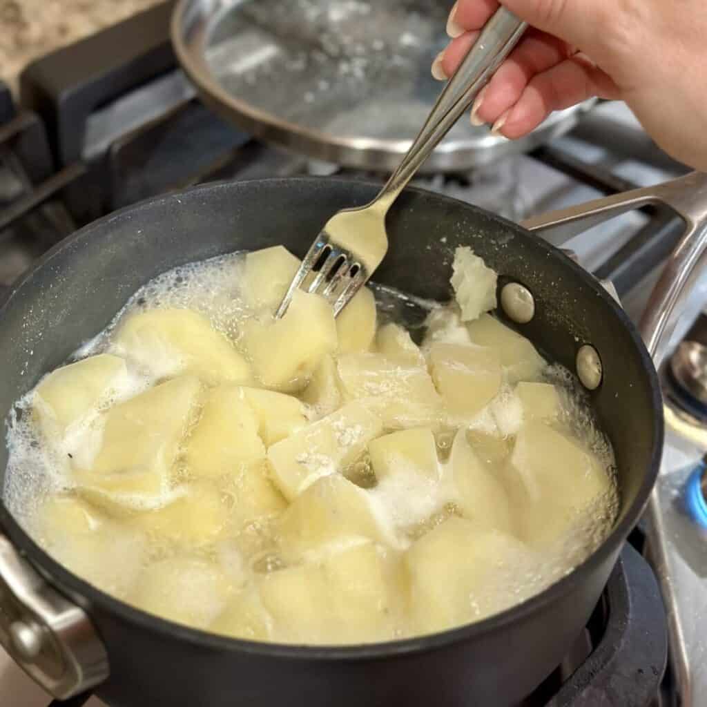 Fork testing potatoes in a pan.