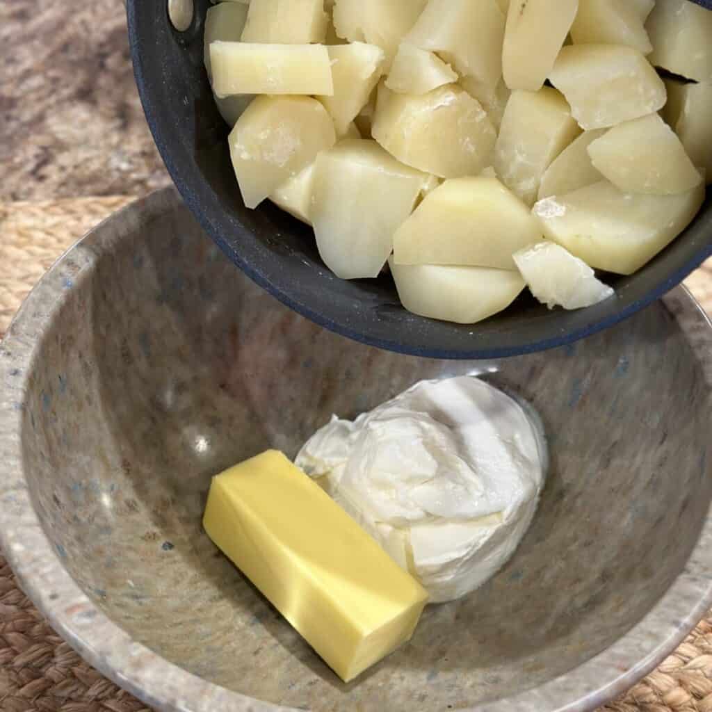 Adding potatoes to a bowl of butter and sour cream.