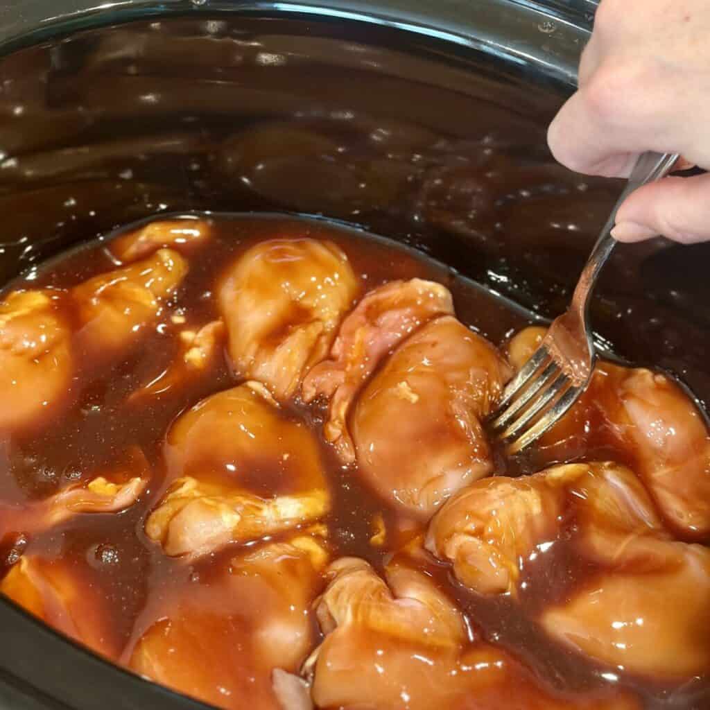 Adding sauce to the top of chicken in a crockpot.