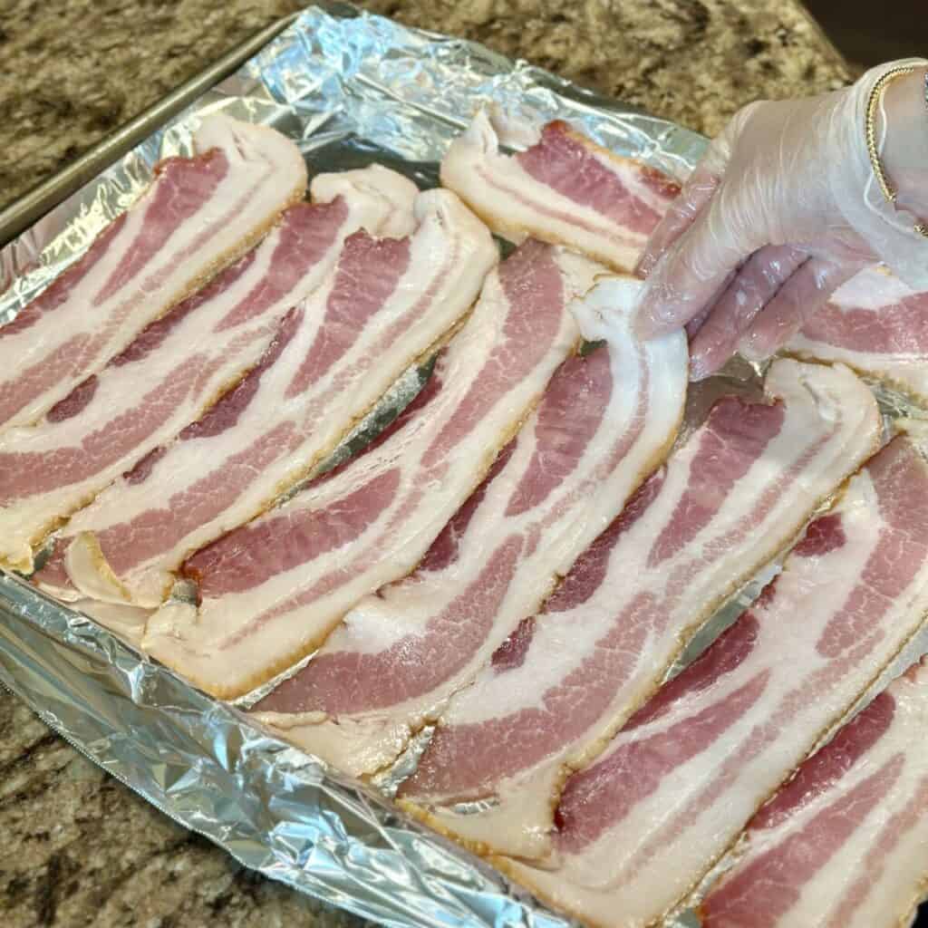 Placing bacon on a sheet pan.