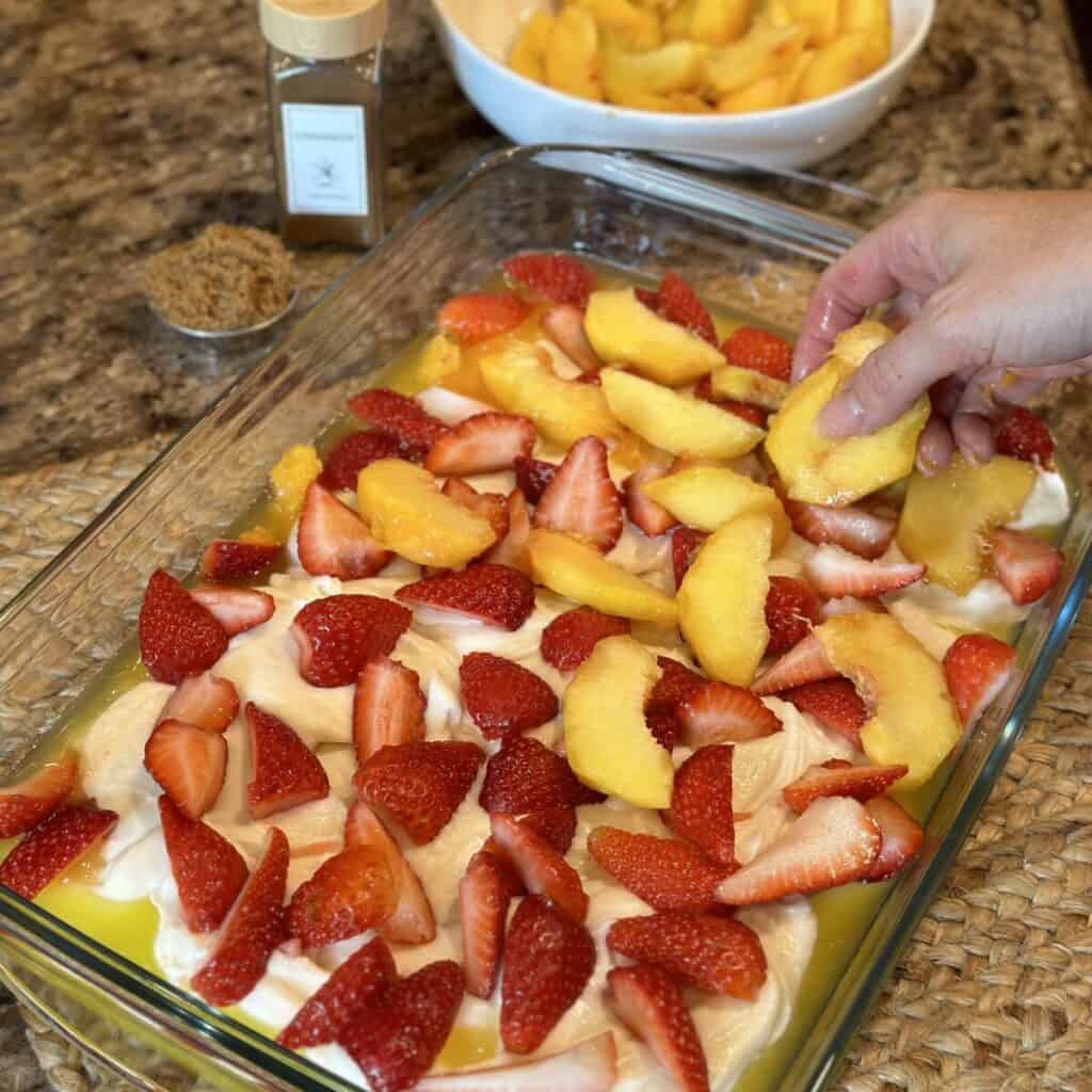 Adding peaches to a cobbler.