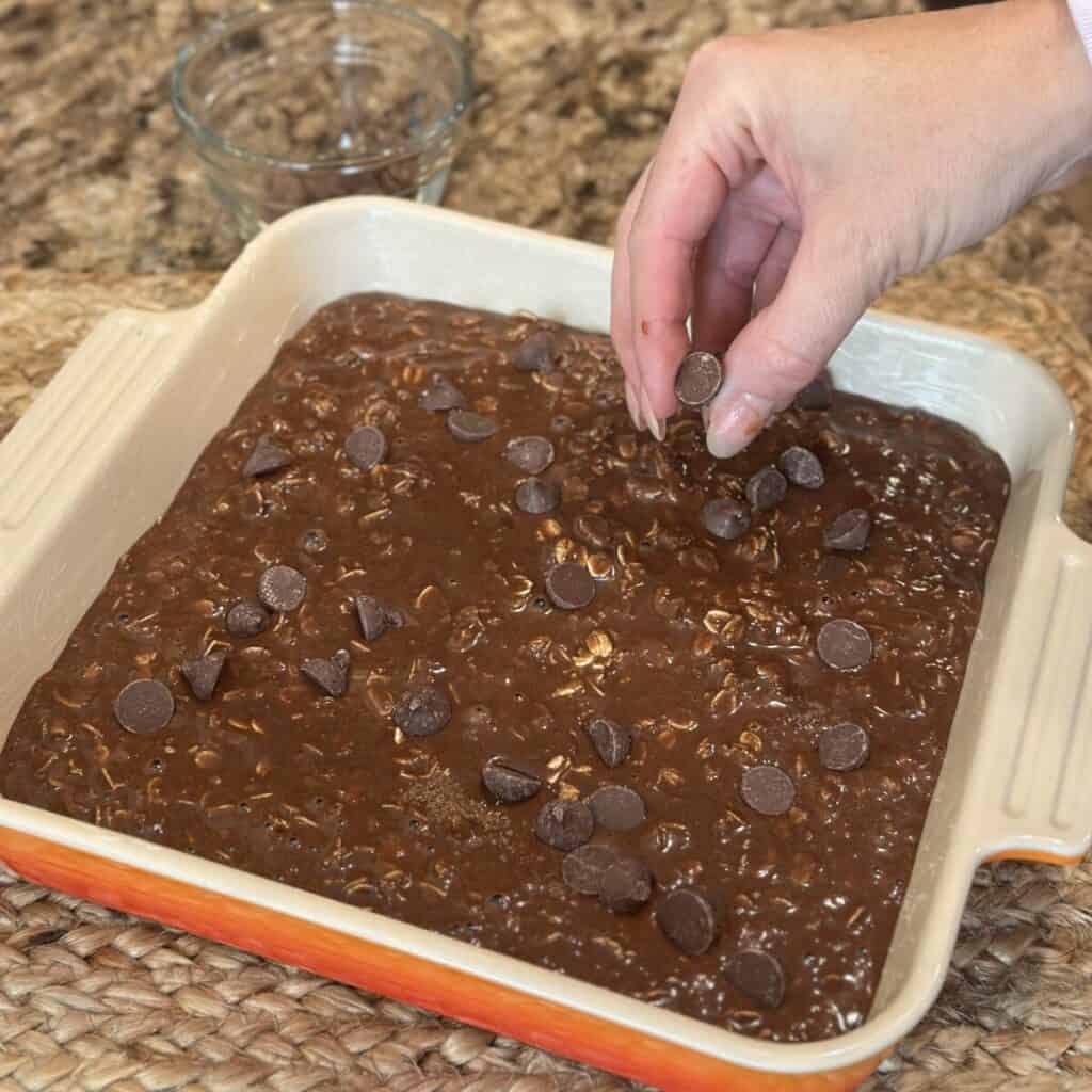 Adding chocolate chips to the top of chocolate oatmeal.