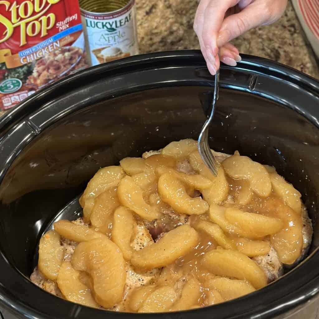 Adding apples to the top of pork chops in a crockpot.