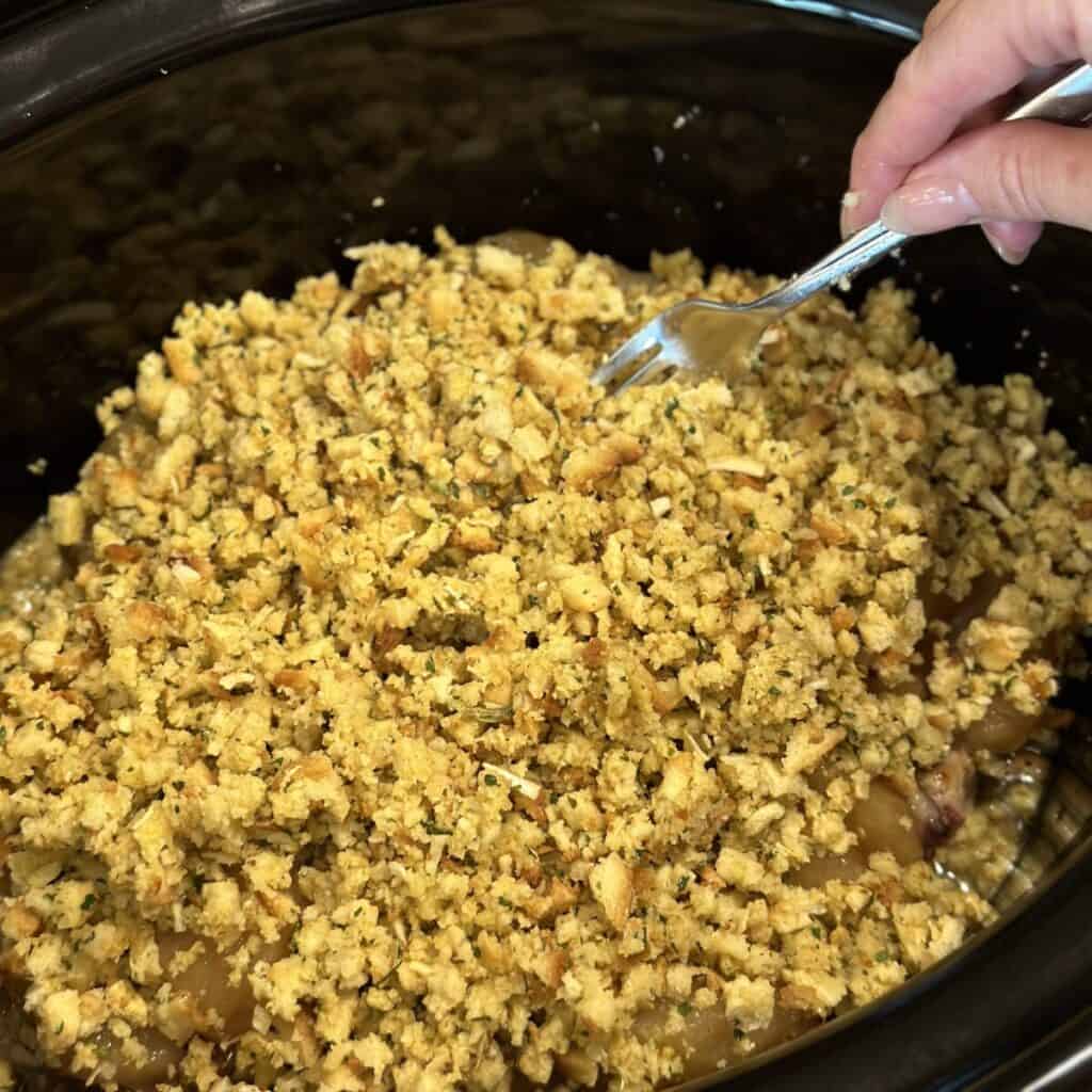 Adding stuffing to the top of pork chops in a crockpot.