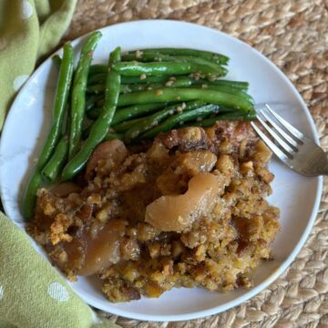 Slow cooker pork chops and apples on a plate with green beans.