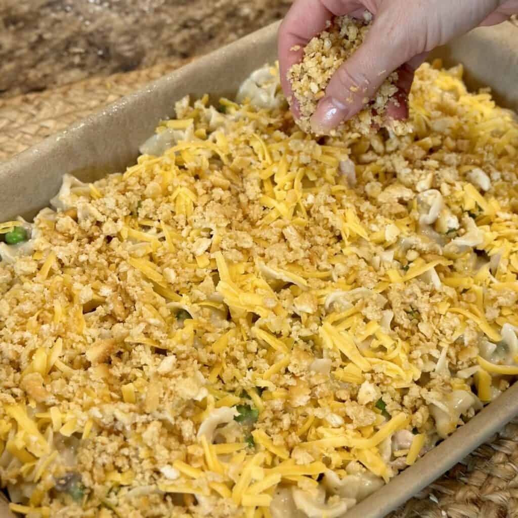 Sprinkling breadcrumbs on a tuna noodle casserole.