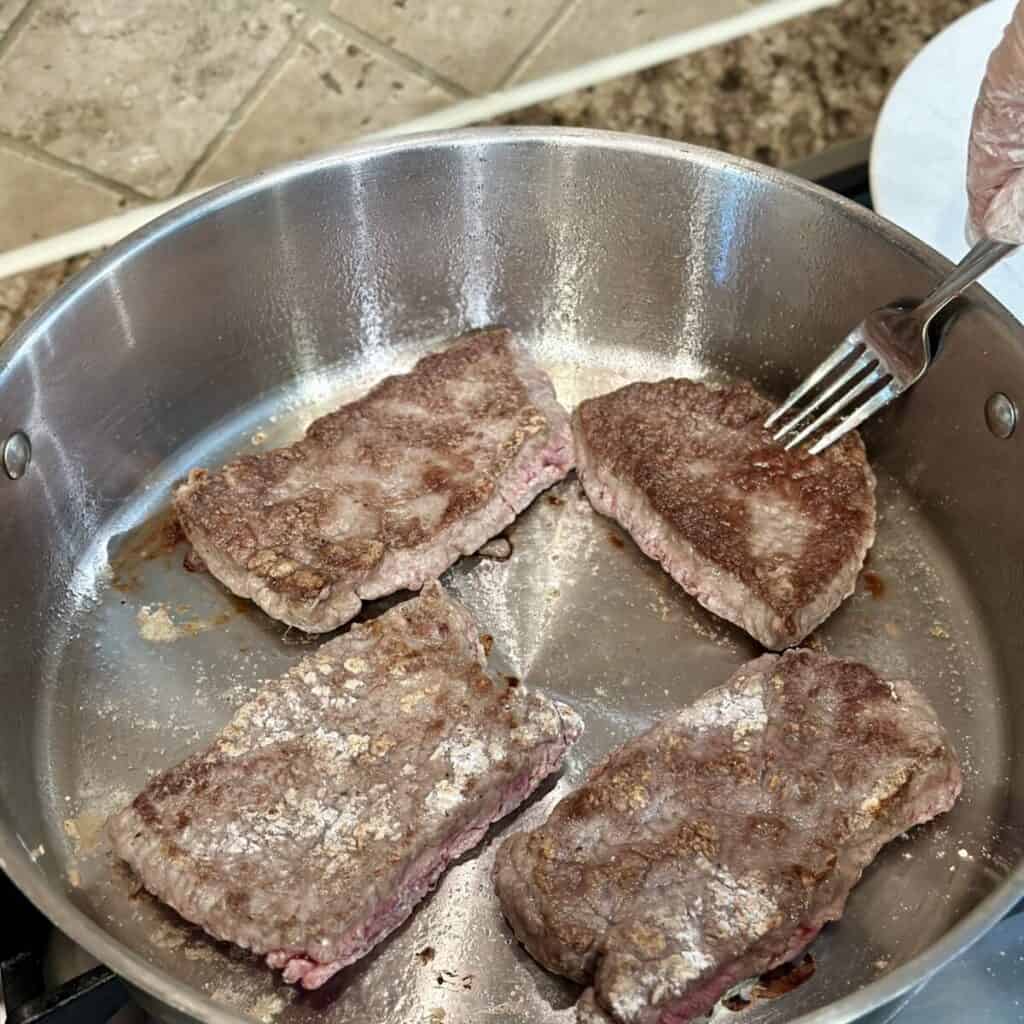 Searing round steak in a skillet.