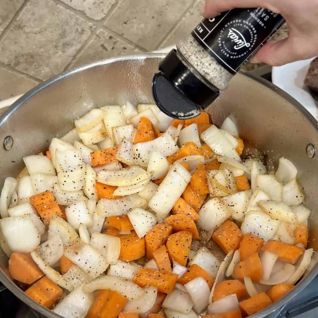 Seasoning onions and carrots in a skillet.