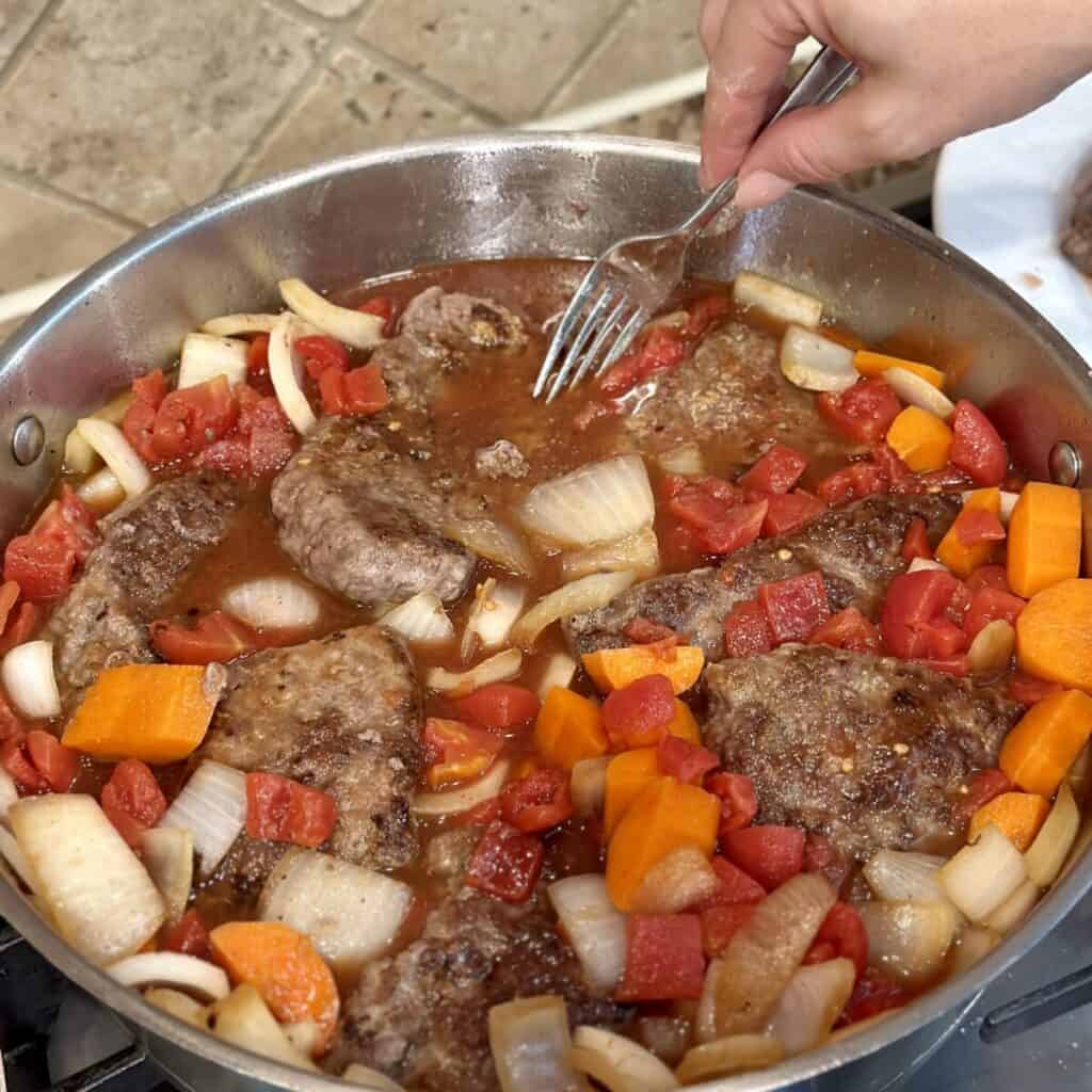 Adding swiss steaks to gravy in a pan.