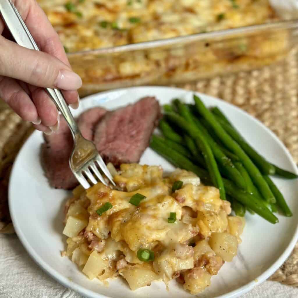 A serving of cooked cheesy ham and potato casserole on a plate.