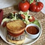 A pizza burger with marinara sauce and salad on a plate.