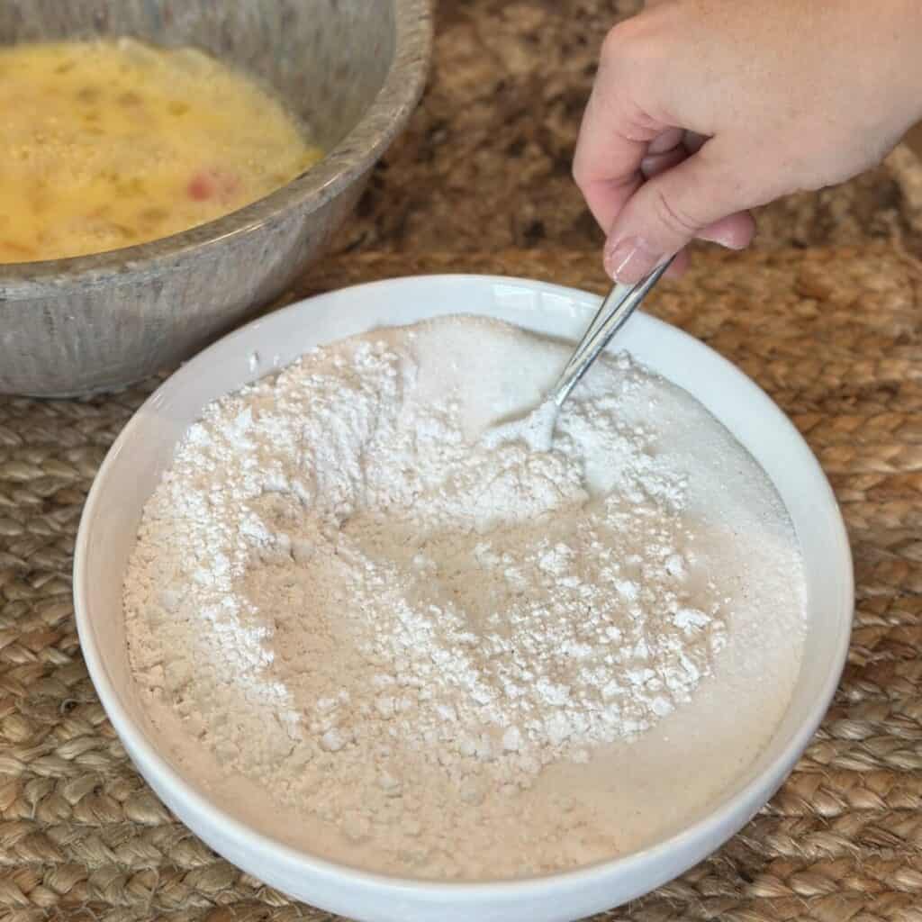 Mixing together dry ingredients for a fruit cocktail cake in a bowl.